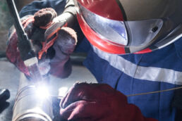 A welder wears a face-shield, protecting them from the bright light of the weld pool.